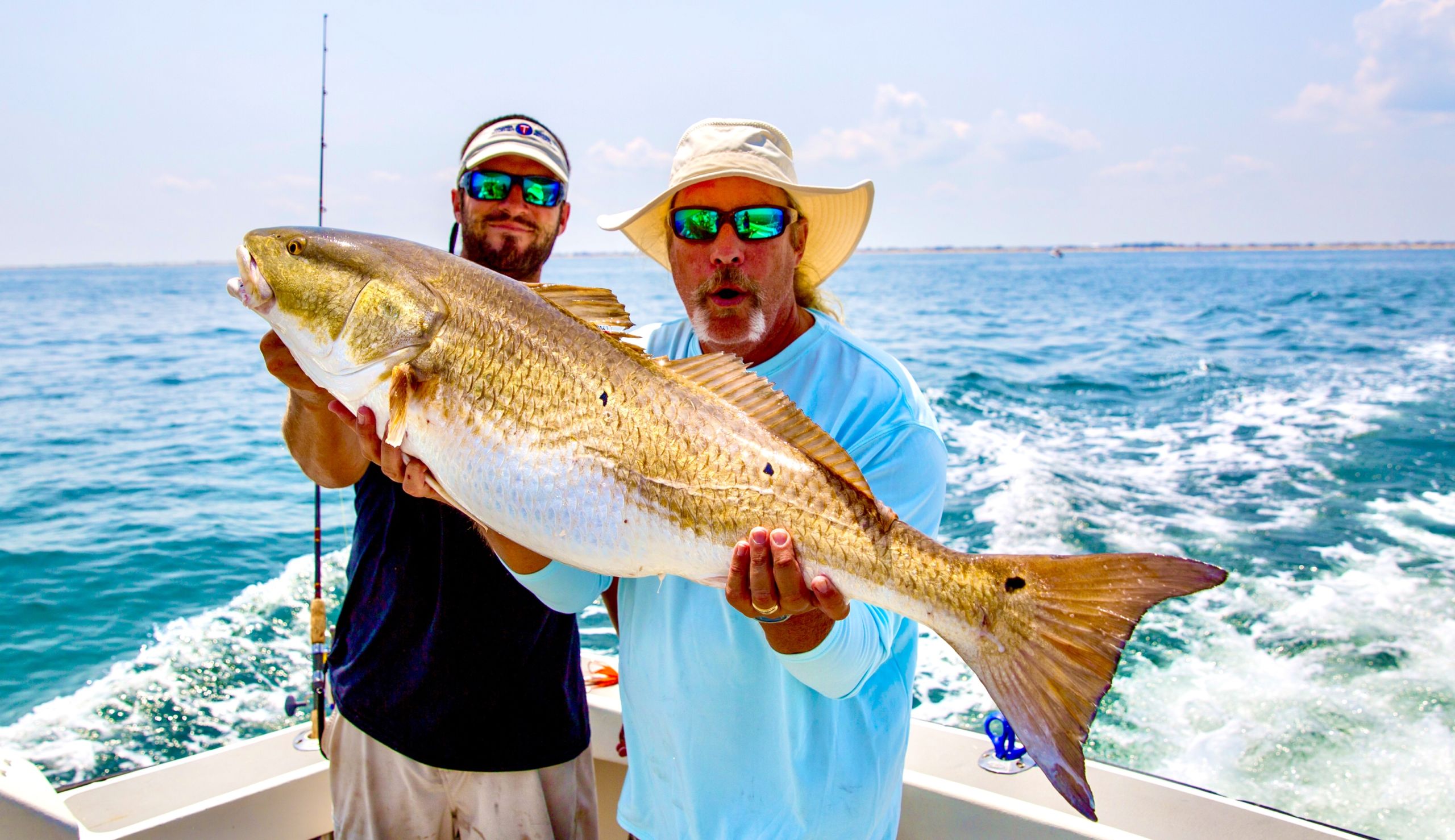 Anglers holding a large red drum on the water